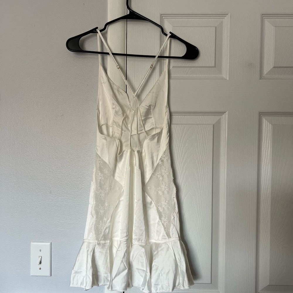 White slip dress with lace details, adjustable straps and ruffle hem